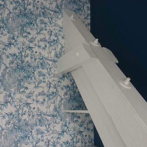 Modern renoviertes Zimmer mit weißem Dachbalken, blau-weißer Mustertapete und dunkelblau gestrichener Akzentwand.