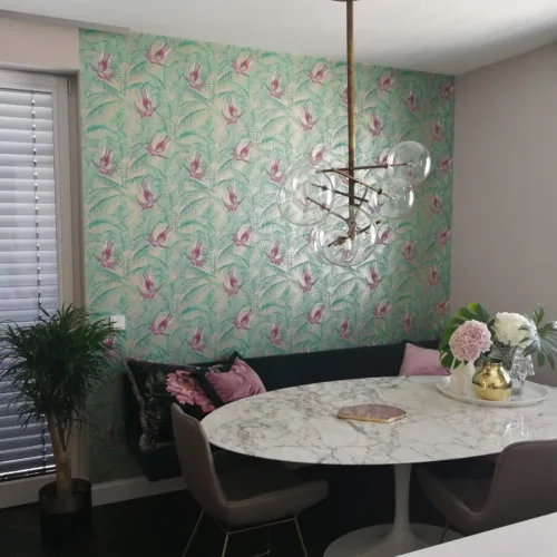 Eine hochwertige Designertapete mit einem detailreichen Muster aus tropischen Vögeln und Palmwedeln in Türkis und Rosa, professionell an der Akzentwand eines stilvollen Essbereichs angebracht.